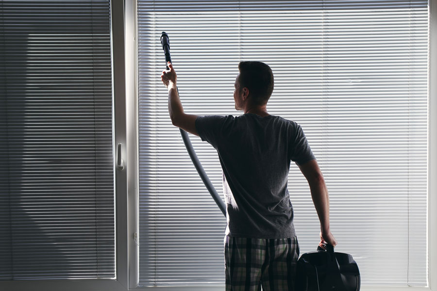 Homme qui nettoie ses stores avec un aspirateur, Stores Chablais SA